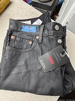 Front and top detail of black Levi 501 jeans with button fly, metal buttons visible, tag attached.