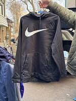 Front view of a black Nike pullover hoodie showing the large white swoosh logo on chest, front kangaroo pocket, and hood with drawstrings.