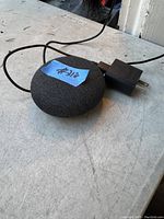 Google Nest Mini portable speaker with attached power adapter and cable shown on a gray surface.