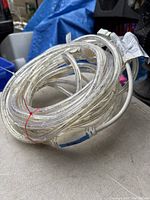 Coiled clear rope light with white power cord and plug shown outdoors on a gray surface with blue tarps and other items in background.