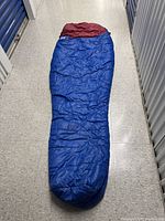 Full length view of single sleeping bag laid flat on floor, showing blue exterior and red interior.