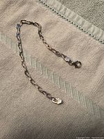 Full length view of the silver chain bracelet laid out on a textured fabric surface, showing the design and length.
