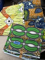 Photo showing three colorful 100% cotton fabrics with distinct African-inspired patterns folded and stacked.