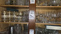 Wide view of wooden shelving unit with various glassware including short glasses with gold trim, stemmed wine and cocktail glasses, and crystal-cut glasses.