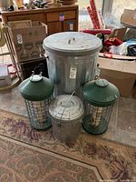 Wide view of the two bird feeders, two metal cans, and surrounding area showing size and condition.