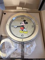 Mickey Mouse clock in box with gold-tone bezel, Mickey's arms serving as hands.