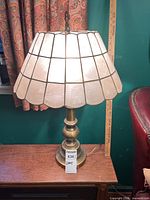 Full view of the lamp on a wooden surface showing the brass base and shell lampshade.