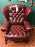 Front view of chair showing tufted back and seat, rolled arms, nailhead trim, caster legs