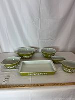 Front view of entire set of 6 Pyrex items showing all bowls and casserole dish with green daisy pattern on plain white table and backdrop.