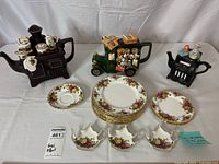 Three novelty teapots, plates and tea bag holders on backdrop