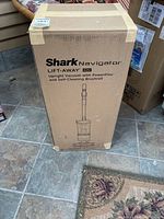 Box of a Shark Navigator Lift-Away ADV upright vacuum cleaner with PowerFins and self-cleaning brushroll, showing front view with brand and model printed.