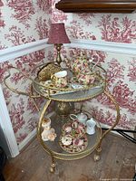 Front view of gold rope-twist metal cart on casters displaying lamp, china set and decor