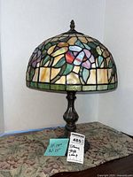 Full view of Tiffany style lamp on a carpeted surface with a handwritten note showing dimensions 15"H x 15"W and a tag indicating 'Tiffany Style Lamp'