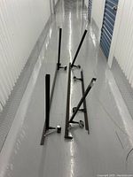 Two black metal box spring bed rails with caster wheels attached on a smooth floor in a storage facility hallway.