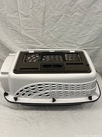 White plastic cat carrier with brown lid featuring ventilation slats and multiple secure black twist latches around the edge. Taken against a neutral backdrop showing the top and side views.