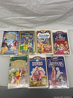 Front view of 7 Disney VHS movie covers laid out flat including Sleeping Beauty, Peter Pan (sealed), Snow White, Alice in Wonderland, Winnie the Pooh, Dumbo, and The Aristocats.