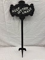 Front view of black cast iron double sided sign with white embossed "Keep Off The Grass" text and single stake