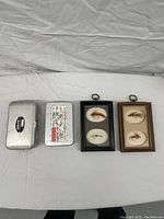 Photo of two vintage metal tackle boxes and two framed fly fishing displays on a white surface.