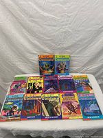 Photo showing 12 paperback Goosebumps books by R.L. Stine placed on a white surface with a white cloth background. Covers show spooky and horror themes typical of the series.