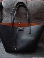 Full view of the Guess tote bag showing black front with brown reversible side on the top edge, on gray couch.