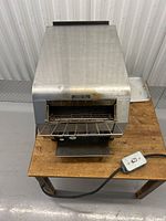 Top front view showing front wire toast rack, heating element area, and attached power cord with inline control box visible on wooden table surface.