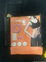 Box showing full product image with purple adjustable weighted hula hoop and a fitness model on the cover.