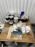 Wide shot of the table showing black metal candle tins, wooden wicks, wick sustainers, and small packets of wick stickers.