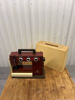Front view of the vintage Husqvarna sewing machine with its beige carrying case on a wooden surface.