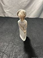 Front view of porcelain figurine of a girl bending forward, showing facial features and dress details, no visible damage.