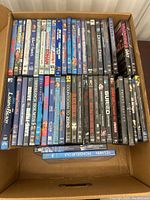Box containing a variety of DVD and Blu-ray movies lined up in two rows. Titles include comedy and drama movies such as 'Donnie Darko', 'Valentine's Day', 'Superbad', and some horror and thriller films.