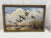 Full view of the framed print depicting ducks taking flight over a marshland with reeds and clouds in the sky.