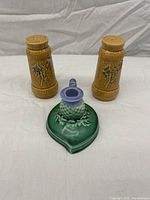Two ceramic salt and pepper shakers with textured wood-like finish and thistle flower relief design, alongside a green heart-shaped ceramic candle stick with purple thistle decoration.