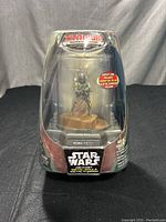 Front view of the die-cast Boba Fett figure in clear plastic display case with Star Wars branding and red sticker.