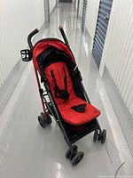 Front angled view of stroller showing red and black seat with cup holder on handle and wheels.