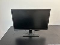 Front view of a black BenQ computer monitor on a stand placed on a black table with a blank screen.