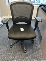 Front view of the black office chair showing seat cushion, armrests, caster wheels, and base.