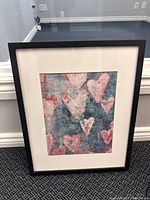 Framed heart wall art piece showing multiple pink and red hearts on a blue textured background.