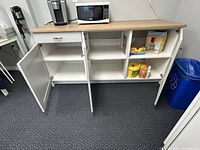 Cabinet doors open showing interior shelf compartments and wood-effect top with appliances