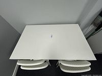 Top-down view showing the white table with four stacked chairs underneath.