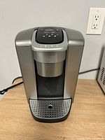 Front view of silver Keurig coffee maker with drip tray and cup holder.