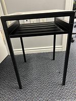 Full view of the tech table showing black metal frame, legs, and slatted lower shelf.