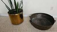 Photo showing the brass planter with snake plant and the large decorative metal pan with iron handles on the floor.