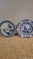Two Delfts Blue plates side by side showing detailed blue and white designs of Dutch rural scenes.