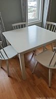 White solid wood square dining table with four chairs around it, showing overall condition and appearance.