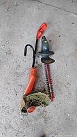 Two electric garden trimmers, one orange grass trimmer with grass debris and one green hedge trimmer.