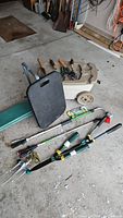 Photo showing rolling garden cart, green cushioned kneeler, black knee pad, pruning shears and long handled shears on concrete floor