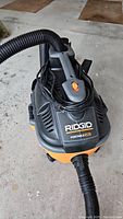 Top view of Ridgid Portable Vacuum Cleaner showing black and orange body with power switch and hose connected.