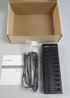 Top-down photo including the USB hub, user manual and USB cable with empty packaging box in the background.