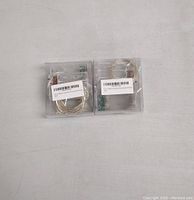 Two battery-operated LED string light packs in clear plastic packaging placed on a light gray surface, each containing a coiled string and battery pack.