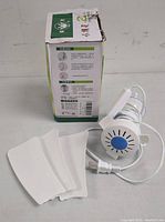 White ceiling fan motor with attached power cord, and three white fan blades arranged beside the motor. The motor has a blue circular vent.